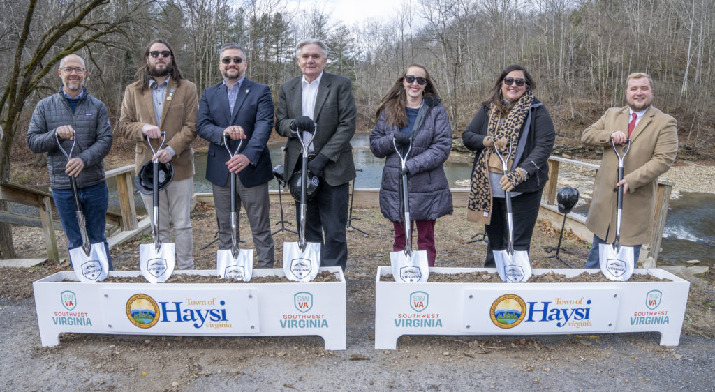 Regional partners stand with shovels and a box full of dirt at the future site of the Haysi Riverwalk.